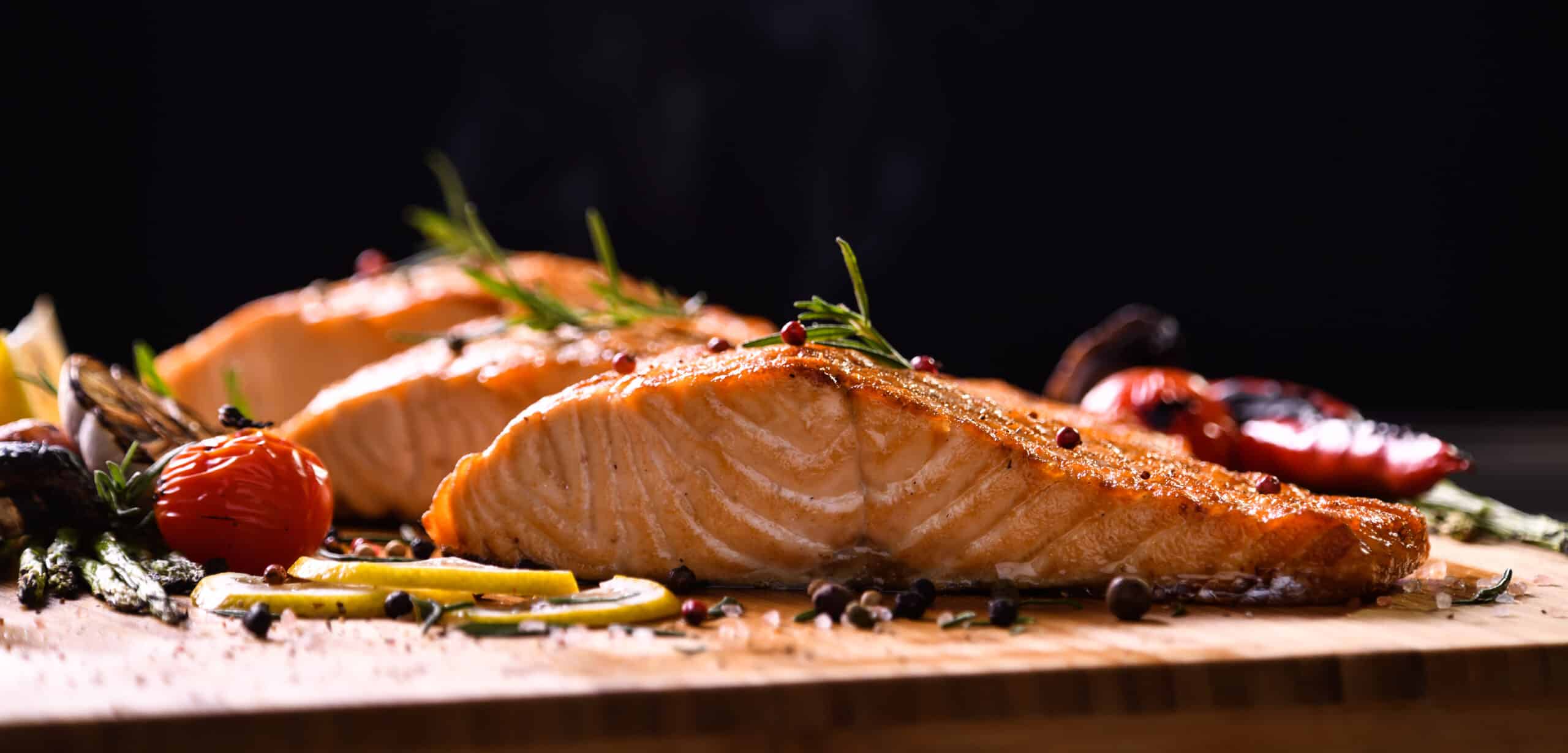Grilled salmon fish and various vegetables on wooden table on black background